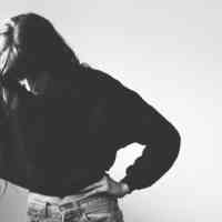 Girl looking down with arm reaching out to nearby window and other hand on hip