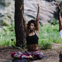 Woman sitting on the ground with her hands in the air, doing yoga in nature