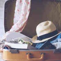 A suitcase filled with a sun hat, flip flops, passport, books, and scarf on top of a bed