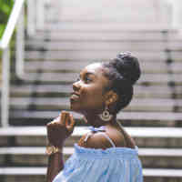 Woman standing with profile view and fisted hand brought to chin at bottom of outdoor stairs