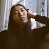a woman leaning with her head on her hand against a white wall