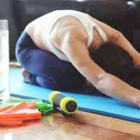 Woman in childs pose on yoga mat with water bottle
