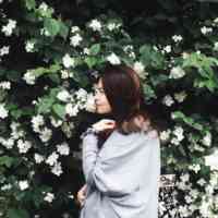 Woman with brown hair standing in front of floral garden wall