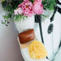 Schmidt's Rose+Vanilla bar soap on the side of a white tub with a loofah and pink floral arrangement as the tub fills up with water