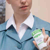 Een vrouw draagt een vintage blauwe jas met een wit overhemd met kraag en een Bergamot + Lime deodorantstick.